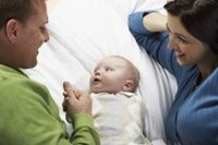 Photo of a baby looking into its father's eyes with the mother smiling at them.