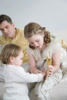 Photo of a baby looking intently at a picture book with sister and father looking on.