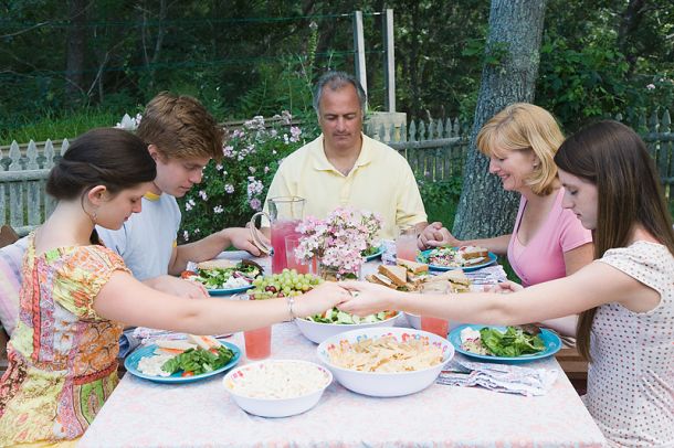 Photo of family holding hands praying before a meal outdoors