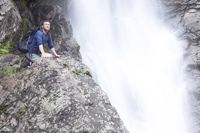 Photo of a man on his knees next to a waterfall, looking with wonder, illustrating praising God.