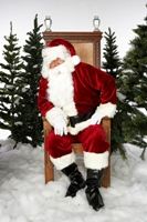 Santa Claus sitting on a chair surrounded by Christmas trees and snow